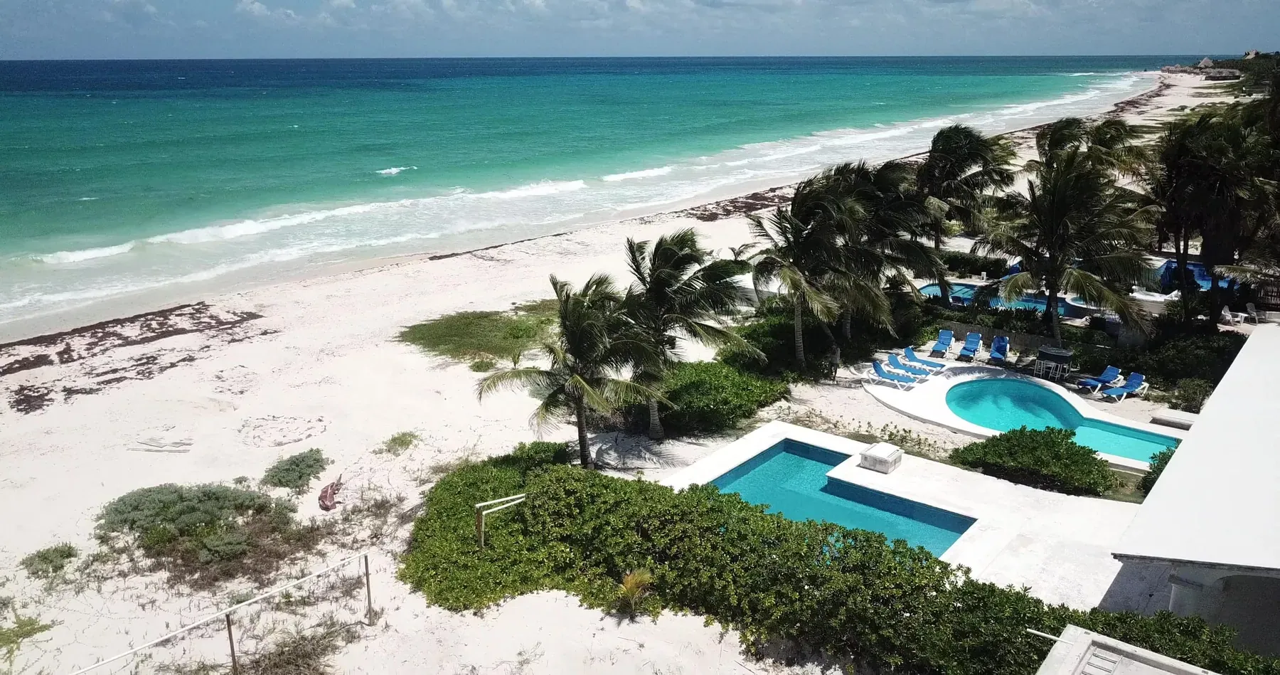 The coast from the air: white sand, palms and the villas' pools